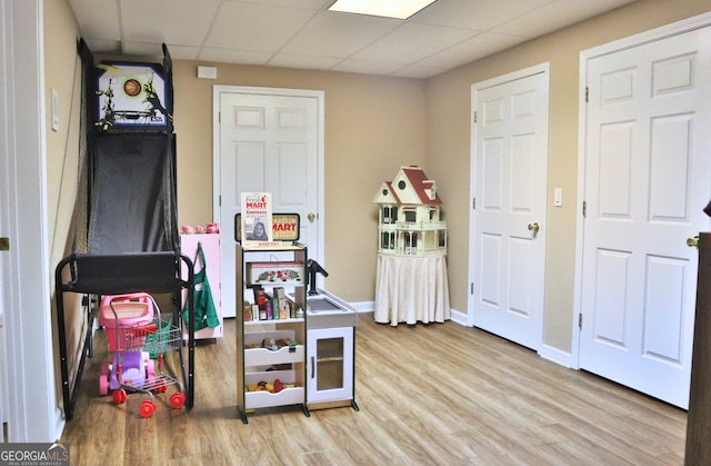 rec room with a paneled ceiling, baseboards, and wood finished floors