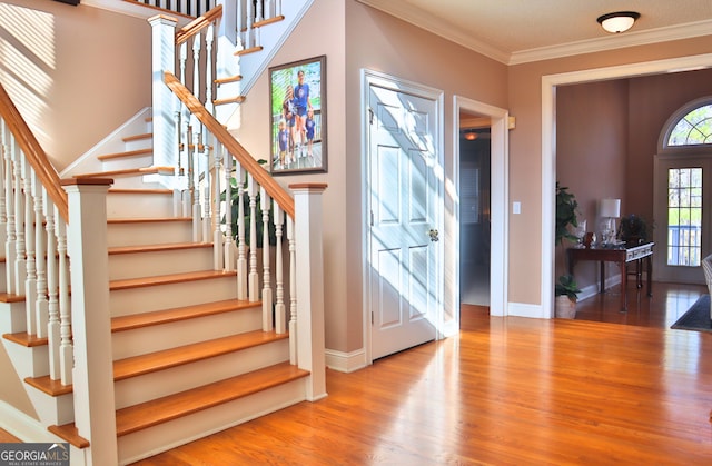 foyer with stairs, ornamental molding, wood finished floors, and baseboards