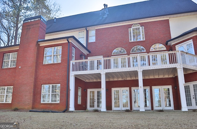 rear view of house with french doors, brick siding, a chimney, and a balcony