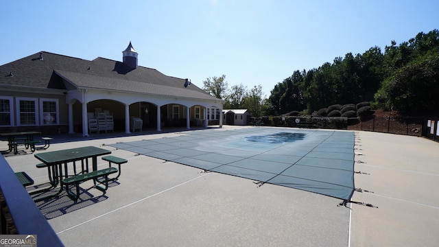 community pool with an outbuilding, a patio area, and fence