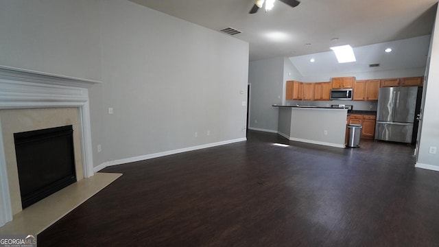 kitchen with stainless steel appliances, dark countertops, open floor plan, and vaulted ceiling with skylight