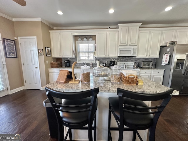 kitchen featuring dark wood-style flooring, crown molding, backsplash, white appliances, and a kitchen breakfast bar