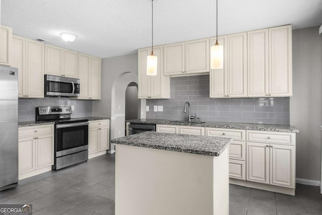 kitchen with arched walkways, a center island, cream cabinets, appliances with stainless steel finishes, and a sink