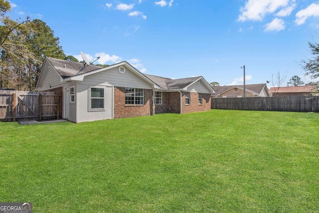 back of house with brick siding, a fenced backyard, and a yard