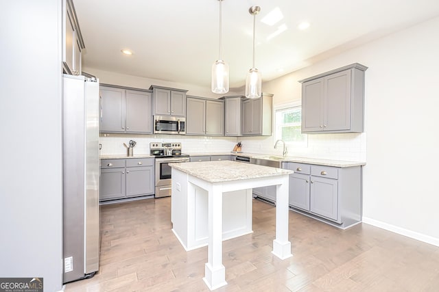 kitchen featuring stainless steel appliances, light wood finished floors, a center island, and gray cabinetry