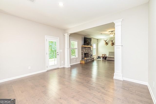 unfurnished living room with baseboards, a ceiling fan, wood finished floors, ornate columns, and a fireplace