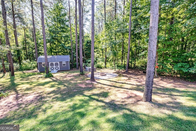 view of yard with a forest view, an outdoor structure, a fire pit, and a storage shed