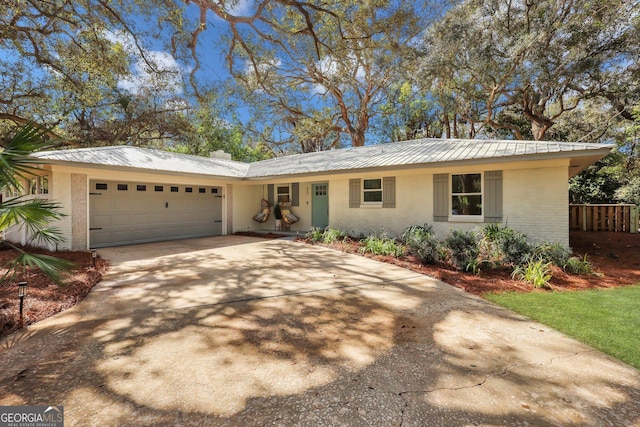 single story home featuring brick siding, metal roof, driveway, and an attached garage