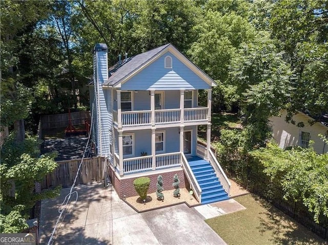 view of front of home featuring a balcony, covered porch, fence, stairs, and a chimney