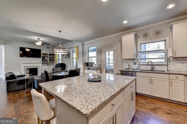 kitchen with a center island, a fireplace, wood finished floors, a sink, and light stone countertops