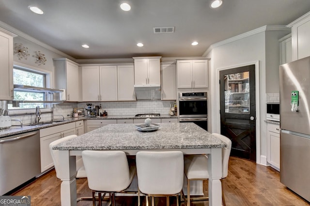 kitchen featuring stainless steel appliances, a sink, visible vents, a center island, and a kitchen bar