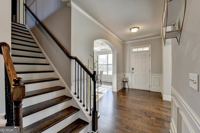 entryway featuring arched walkways, wood finished floors, stairs, ornamental molding, and wainscoting