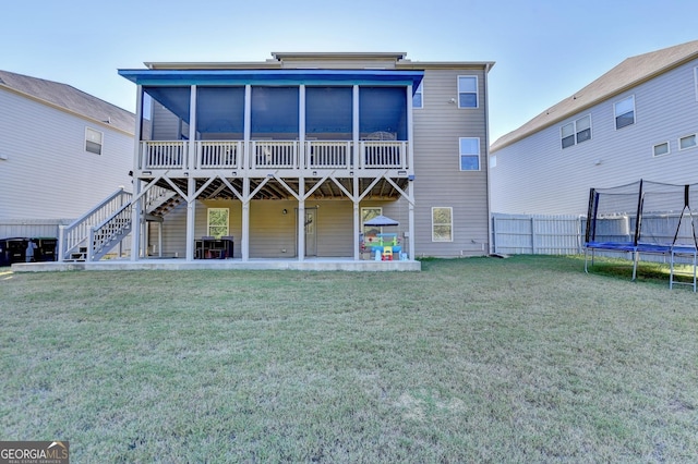 rear view of house featuring a trampoline, a sunroom, a patio area, and a lawn