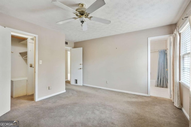 unfurnished bedroom with a textured ceiling, a spacious closet, carpet flooring, and baseboards