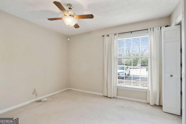 spare room featuring light carpet, ceiling fan, baseboards, and a healthy amount of sunlight