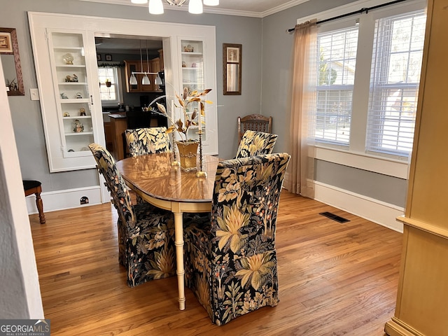 dining room featuring ornamental molding, light wood-type flooring, visible vents, and baseboards