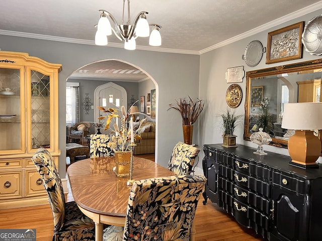 dining room with arched walkways, ornamental molding, light wood-style flooring, and a notable chandelier