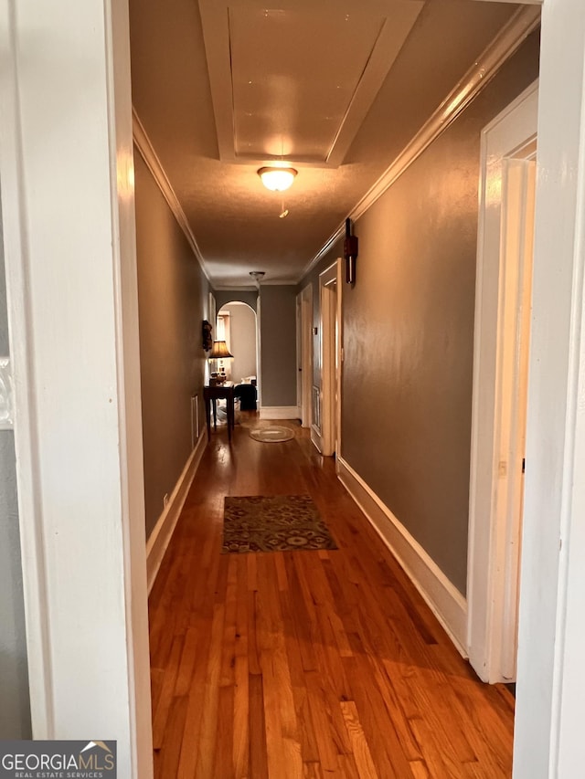 corridor with arched walkways, crown molding, visible vents, wood finished floors, and baseboards