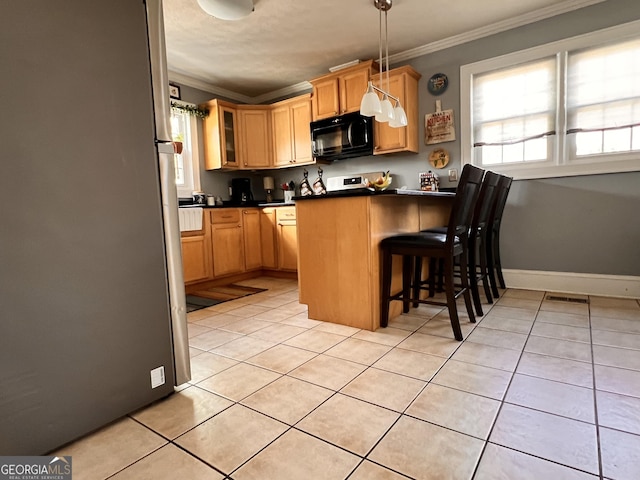 kitchen featuring black microwave, light tile patterned flooring, ornamental molding, freestanding refrigerator, and dark countertops