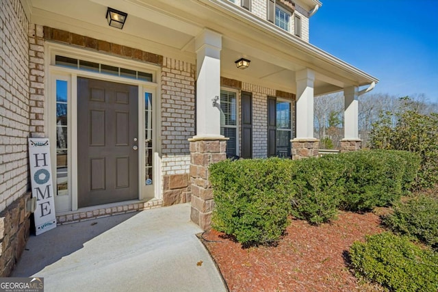 view of exterior entry with brick siding and a porch