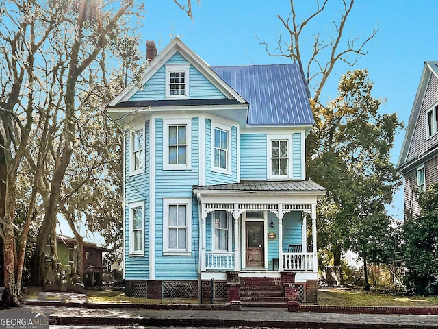 victorian home with covered porch, a chimney, and metal roof