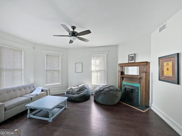 living area with visible vents, baseboards, a fireplace with raised hearth, ceiling fan, and wood finished floors