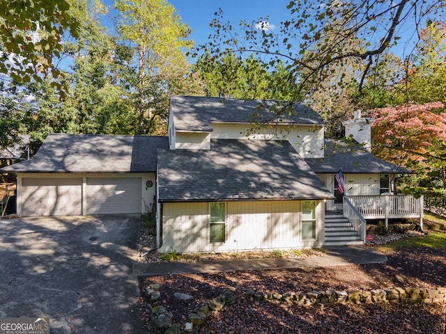 view of front of home featuring aphalt driveway, an attached garage, stairs, a wooden deck, and a chimney