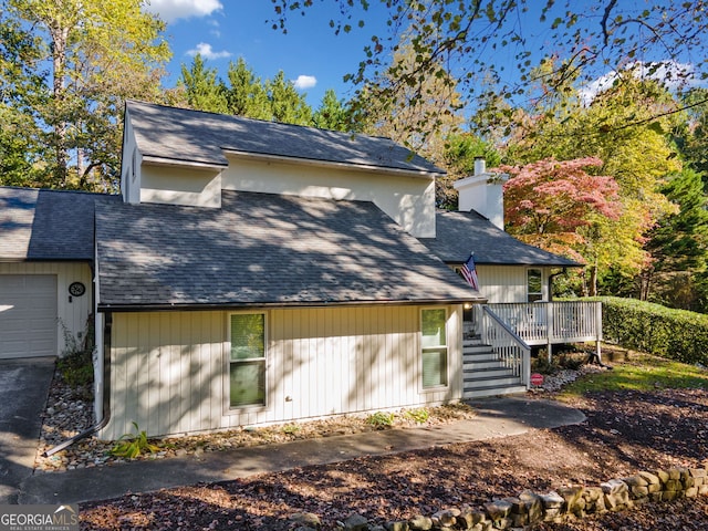 exterior space featuring roof with shingles, a chimney, a deck, a garage, and stairs