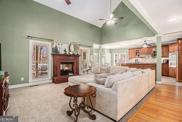 living room featuring high vaulted ceiling, visible vents, baseboards, ornamental molding, and a brick fireplace