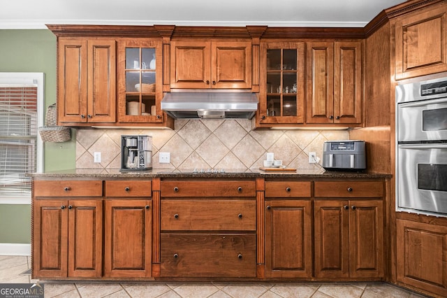 kitchen featuring tasteful backsplash, stainless steel double oven, brown cabinets, and range hood