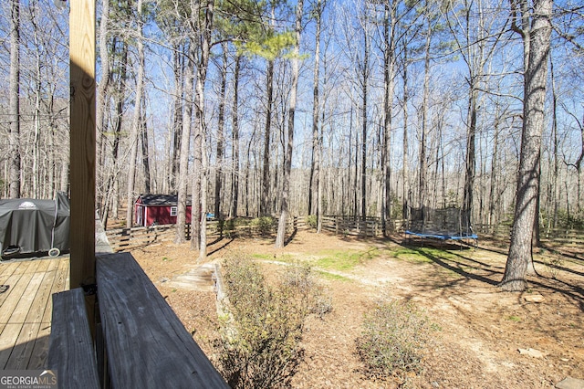 view of yard featuring a trampoline, an outdoor structure, a deck, and a storage unit