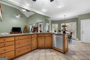 kitchen featuring brown cabinets, light tile patterned flooring, vaulted ceiling, dishwasher, and ceiling fan with notable chandelier