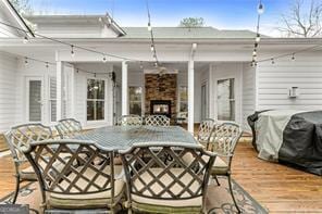 view of patio featuring a warm lit fireplace, a deck, and outdoor dining area