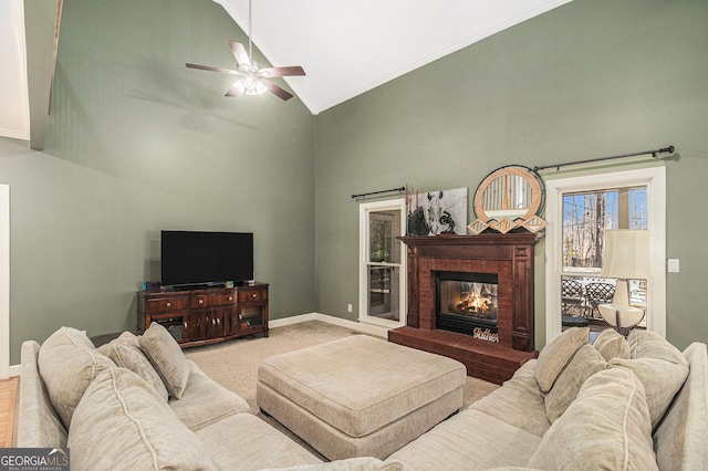 living area featuring baseboards, ceiling fan, carpet flooring, a brick fireplace, and high vaulted ceiling