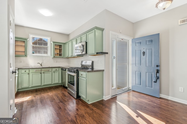 kitchen featuring tasteful backsplash, green cabinetry, dark wood-style flooring, stainless steel appliances, and a sink