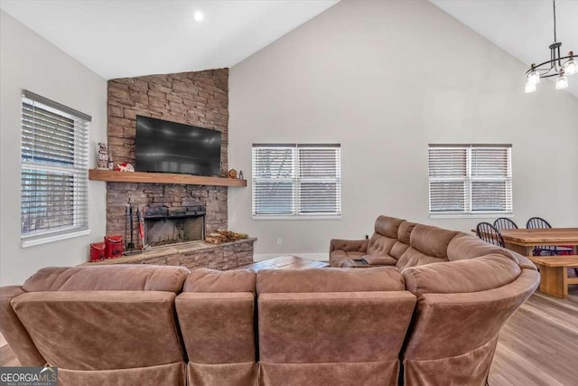 living area with high vaulted ceiling, a stone fireplace, wood finished floors, and an inviting chandelier