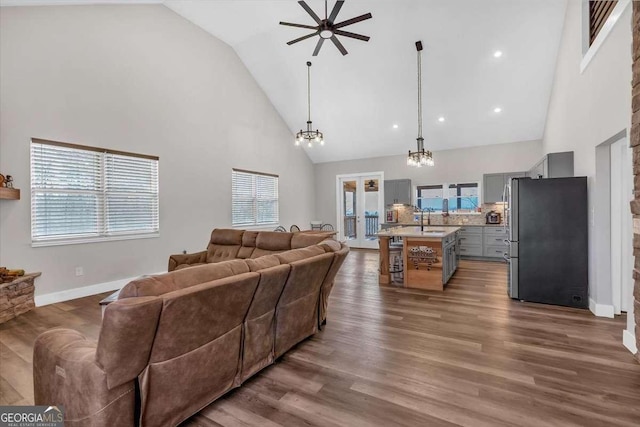 living area featuring ceiling fan with notable chandelier, high vaulted ceiling, wood finished floors, and baseboards