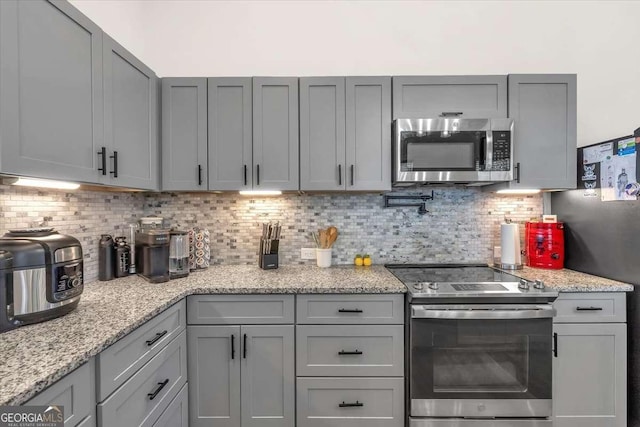 kitchen with stainless steel appliances, light stone counters, gray cabinets, and decorative backsplash