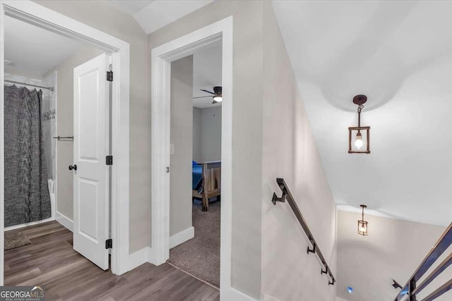 corridor with wood finished floors, an upstairs landing, and baseboards