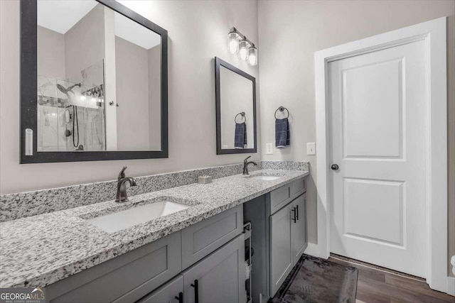 full bathroom with double vanity, wood finished floors, a sink, and a shower with shower door