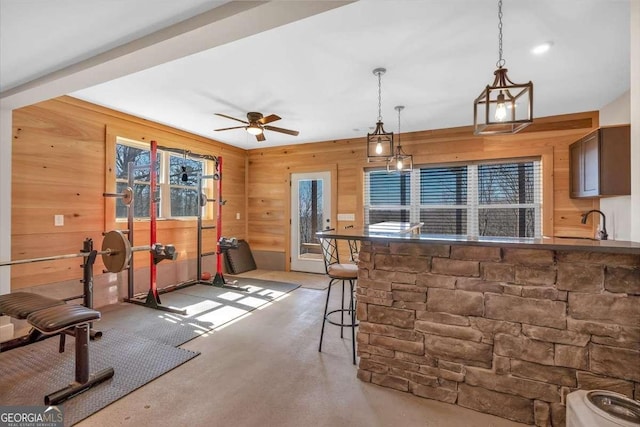 kitchen with a ceiling fan, decorative light fixtures, wooden walls, and a kitchen bar