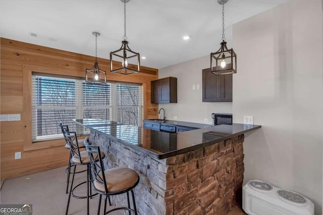 kitchen with pendant lighting, visible vents, a sink, wooden walls, and a kitchen bar