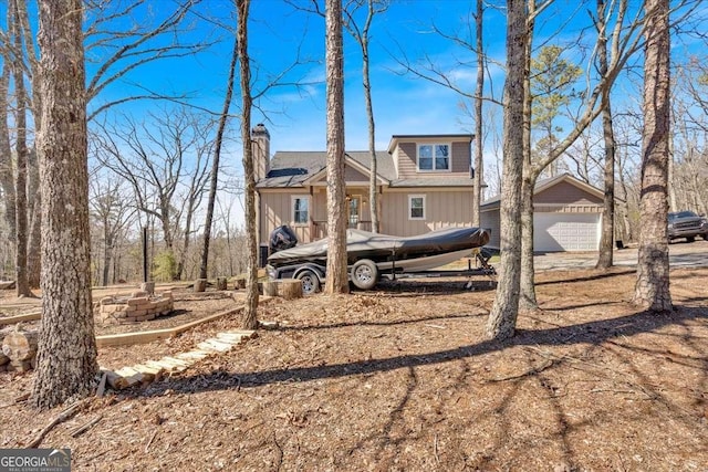 view of front of home with a garage, a fire pit, a chimney, and an outbuilding