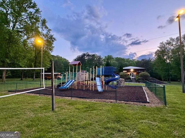 playground at dusk with playground community, a yard, and fence