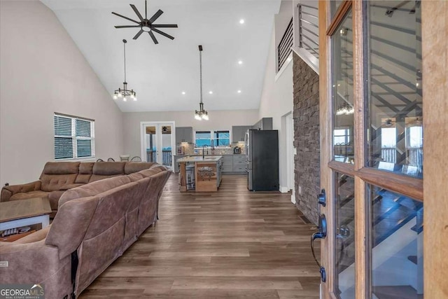 living area featuring dark wood-type flooring, high vaulted ceiling, and ceiling fan with notable chandelier