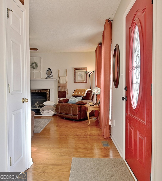 foyer entrance with a textured ceiling, a premium fireplace, light wood-type flooring, and visible vents