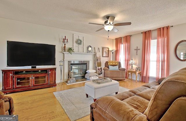 living room featuring a ceiling fan, a tiled fireplace, a textured ceiling, and light wood finished floors