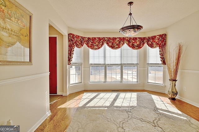 unfurnished dining area featuring a textured ceiling, wood finished floors, and baseboards