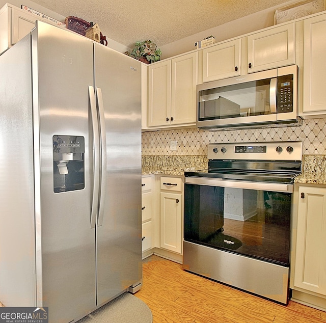 kitchen featuring tasteful backsplash, white cabinets, stainless steel appliances, a textured ceiling, and light wood-type flooring