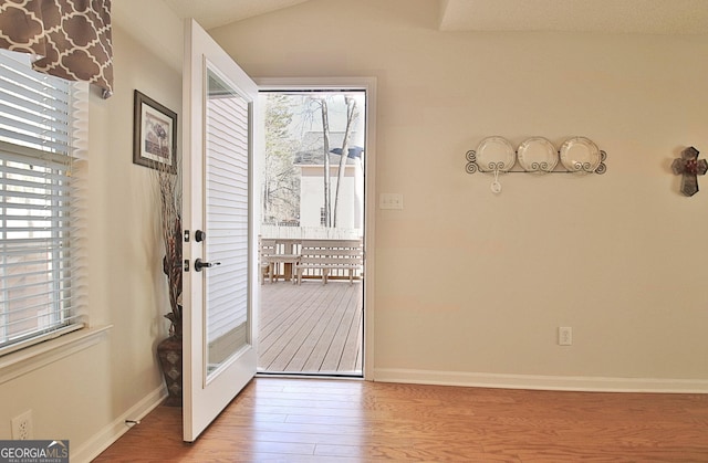 doorway featuring lofted ceiling, baseboards, and wood finished floors